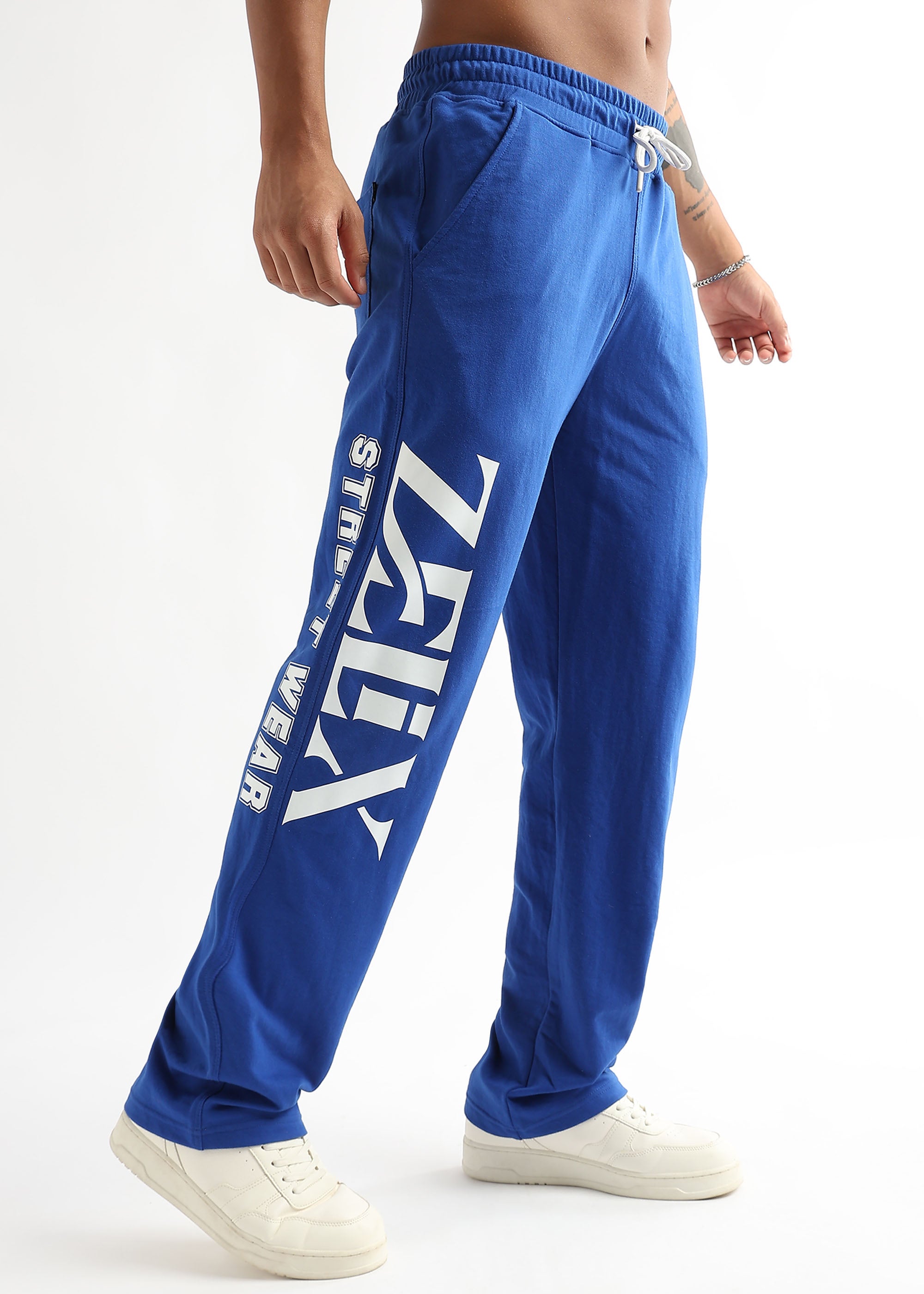 A person wearing royal blue joggers with the brand name 'ZELIX' written across the leg, paired with white sneakers.
