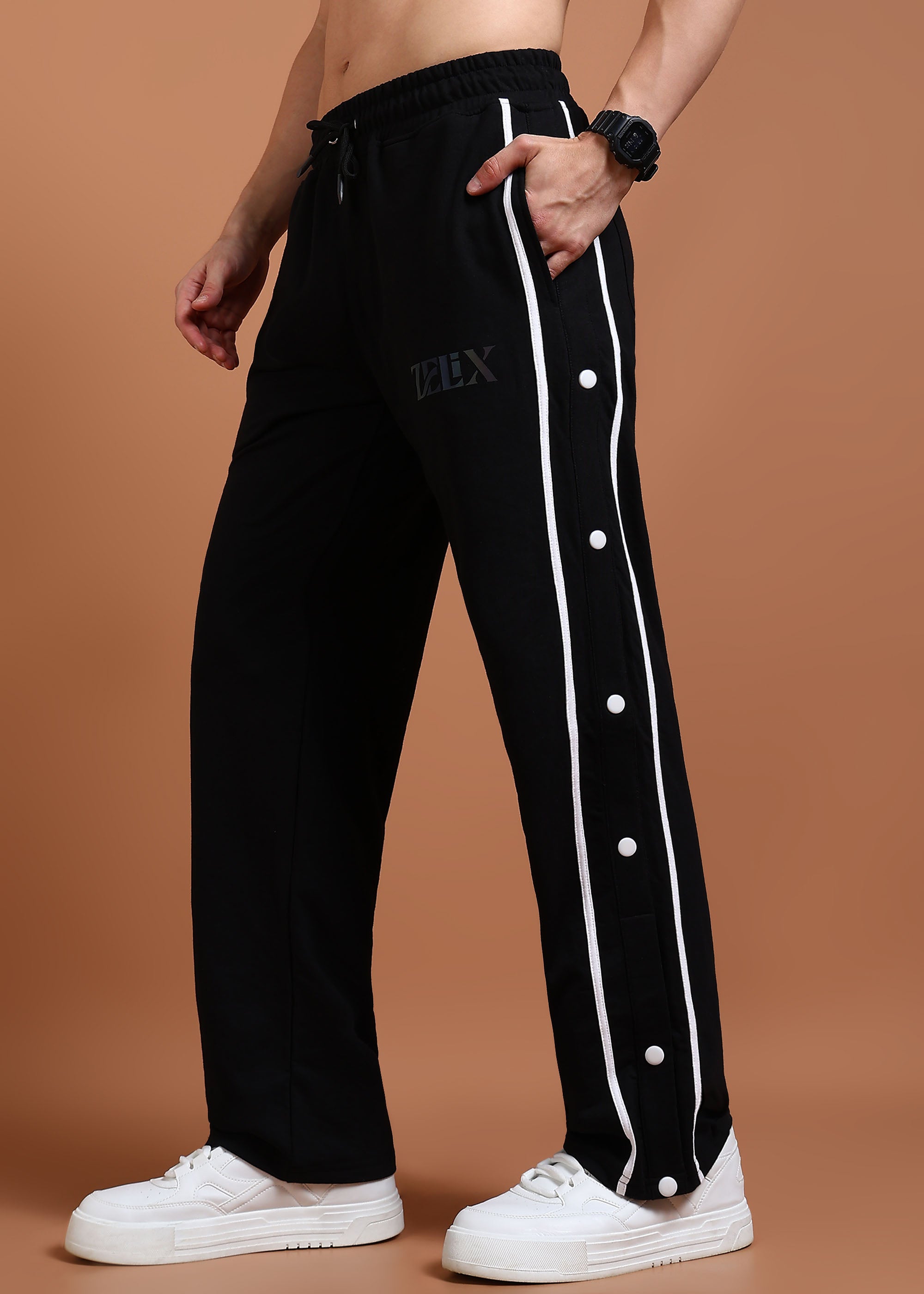 A person wearing black joggers with a white stripe and buttons on the side, paired with white sneakers.