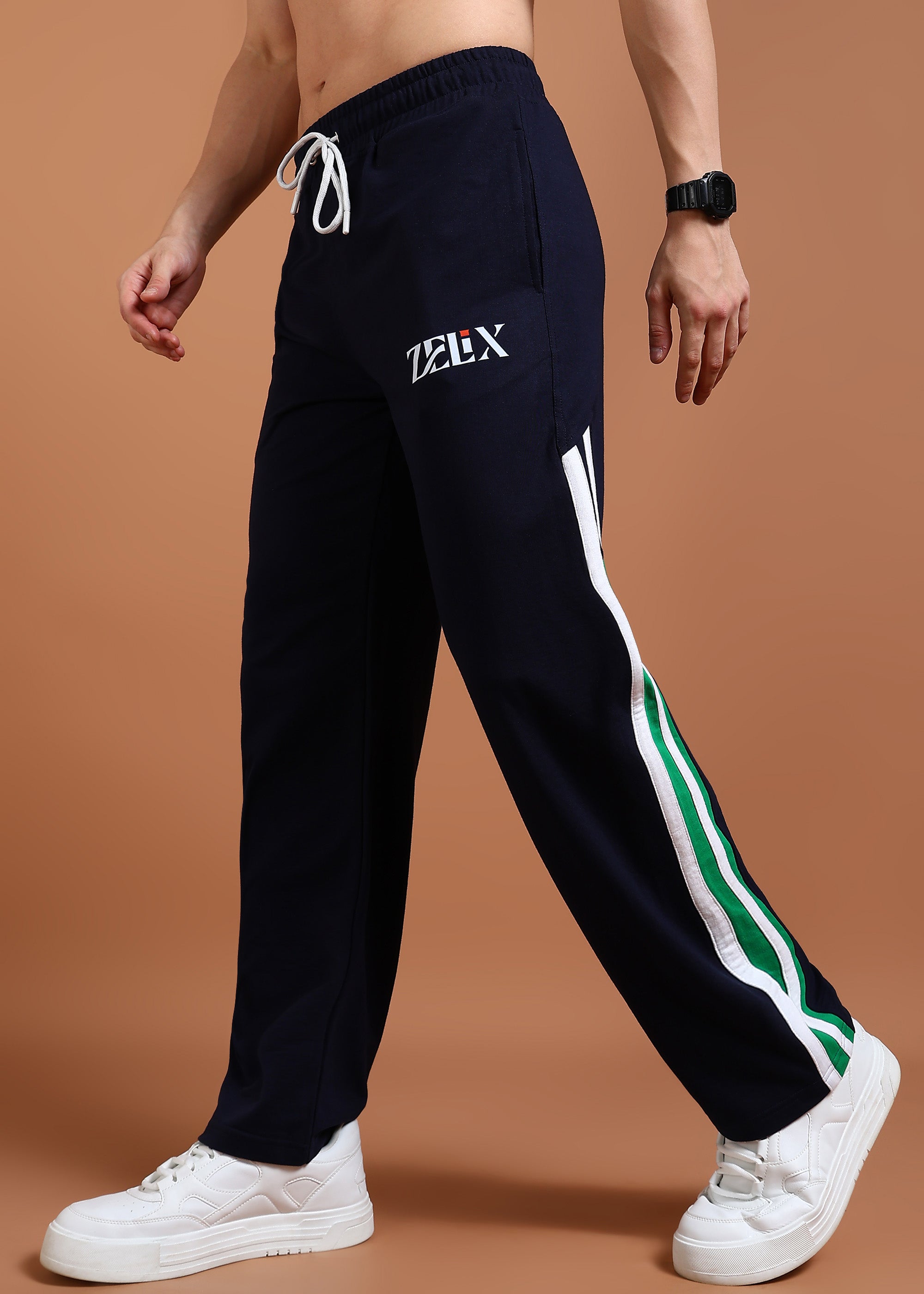 A person wearing navy blue and green baggy joggers with a drawstring waist, branded with 'ZELX' on the left leg, and white sneakers.
