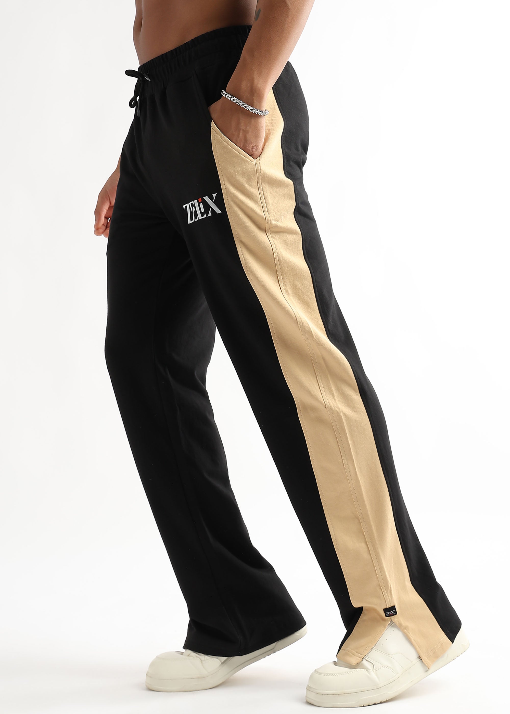 A person wearing black and beige side slit joggers with a drawstring waist, standing on one leg to showcase the side slit feature.