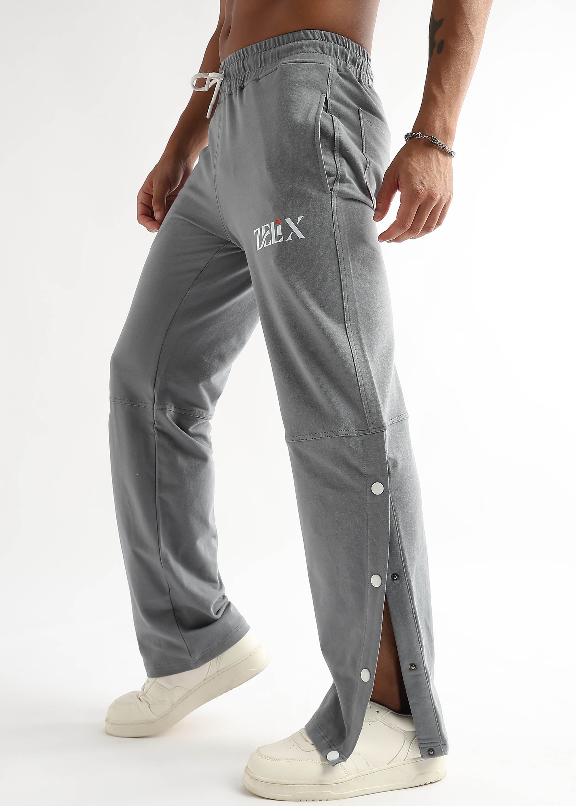 A person wearing grey baggy joggers with a drawstring waistband and side snap details, paired with white sneakers.