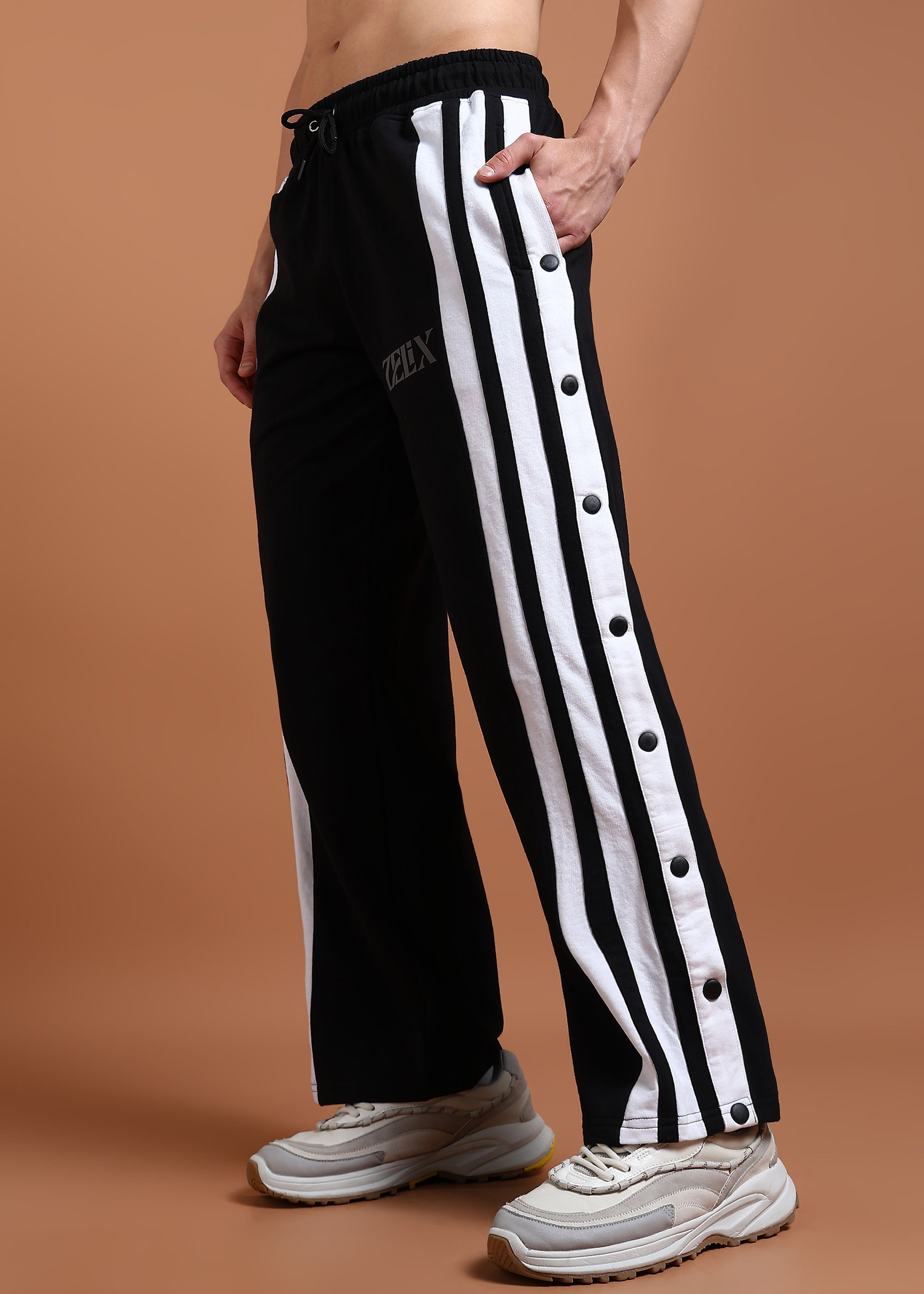 A person wearing black unisex joggers with white stripes and buttons on the side, paired with a black top and white sneakers.