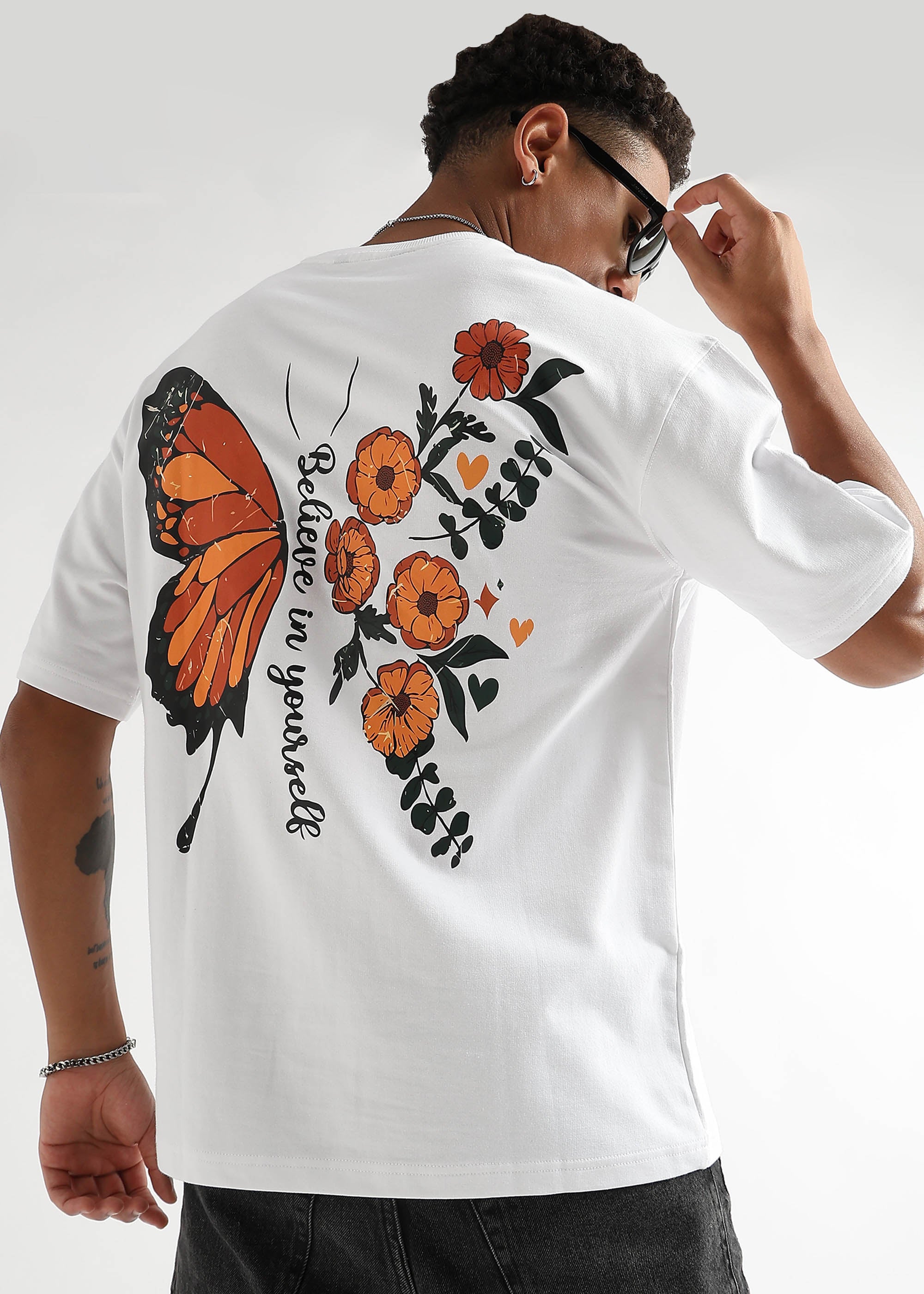 A person wearing an oversized white t-shirt with a graphic of a butterfly and flowers on the back.
