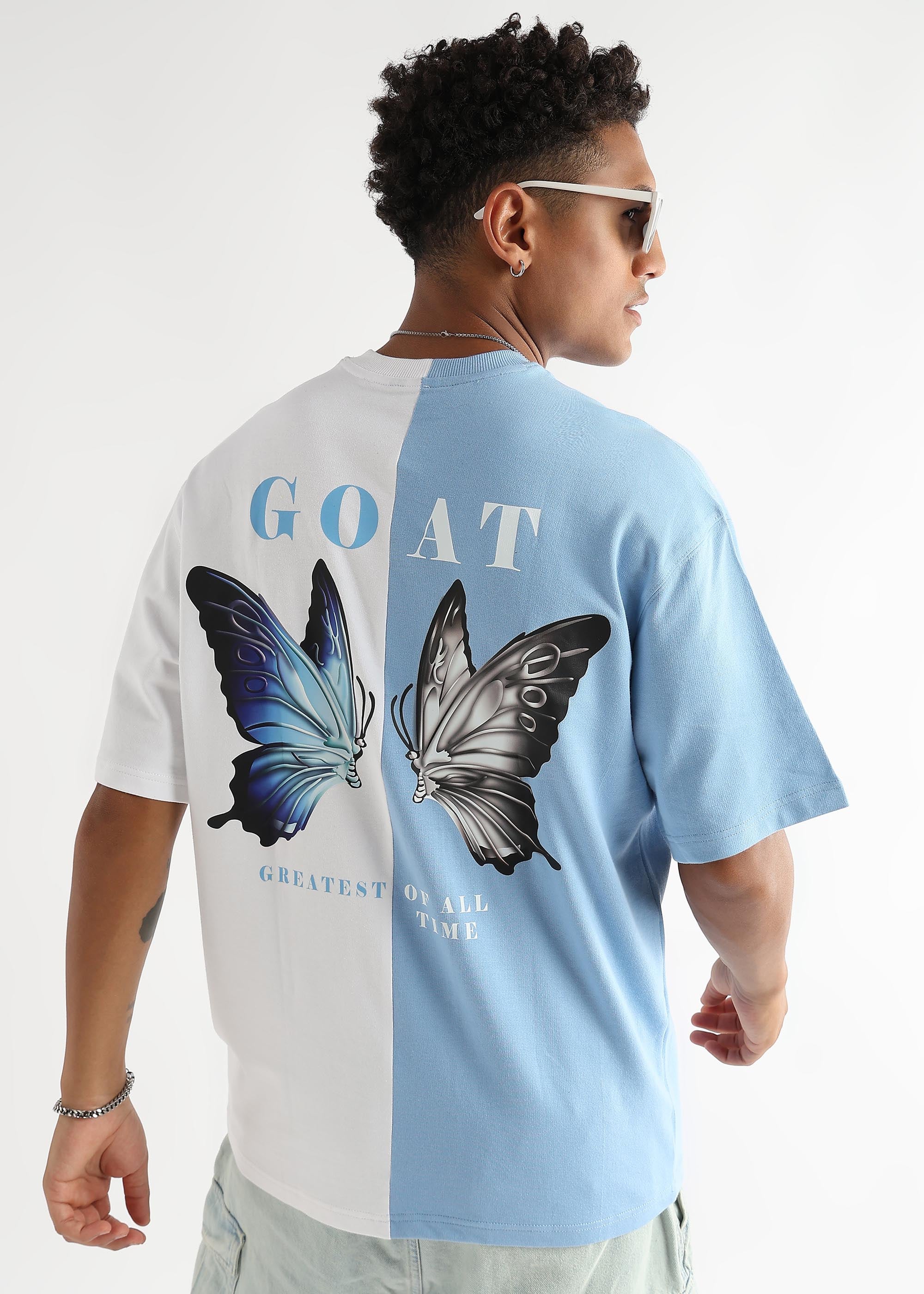 A person wearing an oversized t-shirt with a sky blue and white color scheme. The shirt has a graphic of two butterflies and the text 'GOAT' on the back.