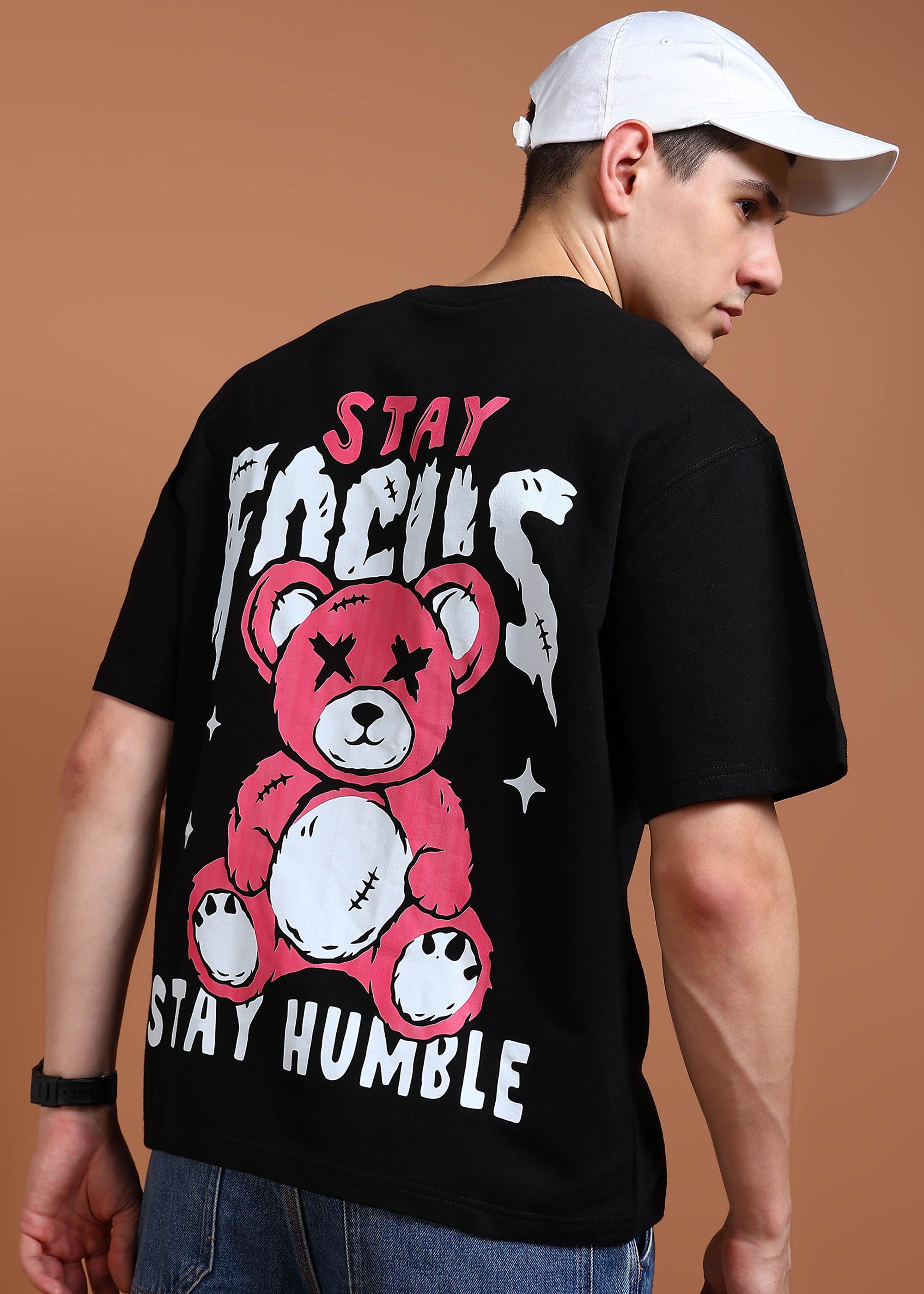 A person wearing a black oversized t-shirt with a graphic that includes a teddy bear and text saying 'STAY FOCUS STAY HUMBLE'.