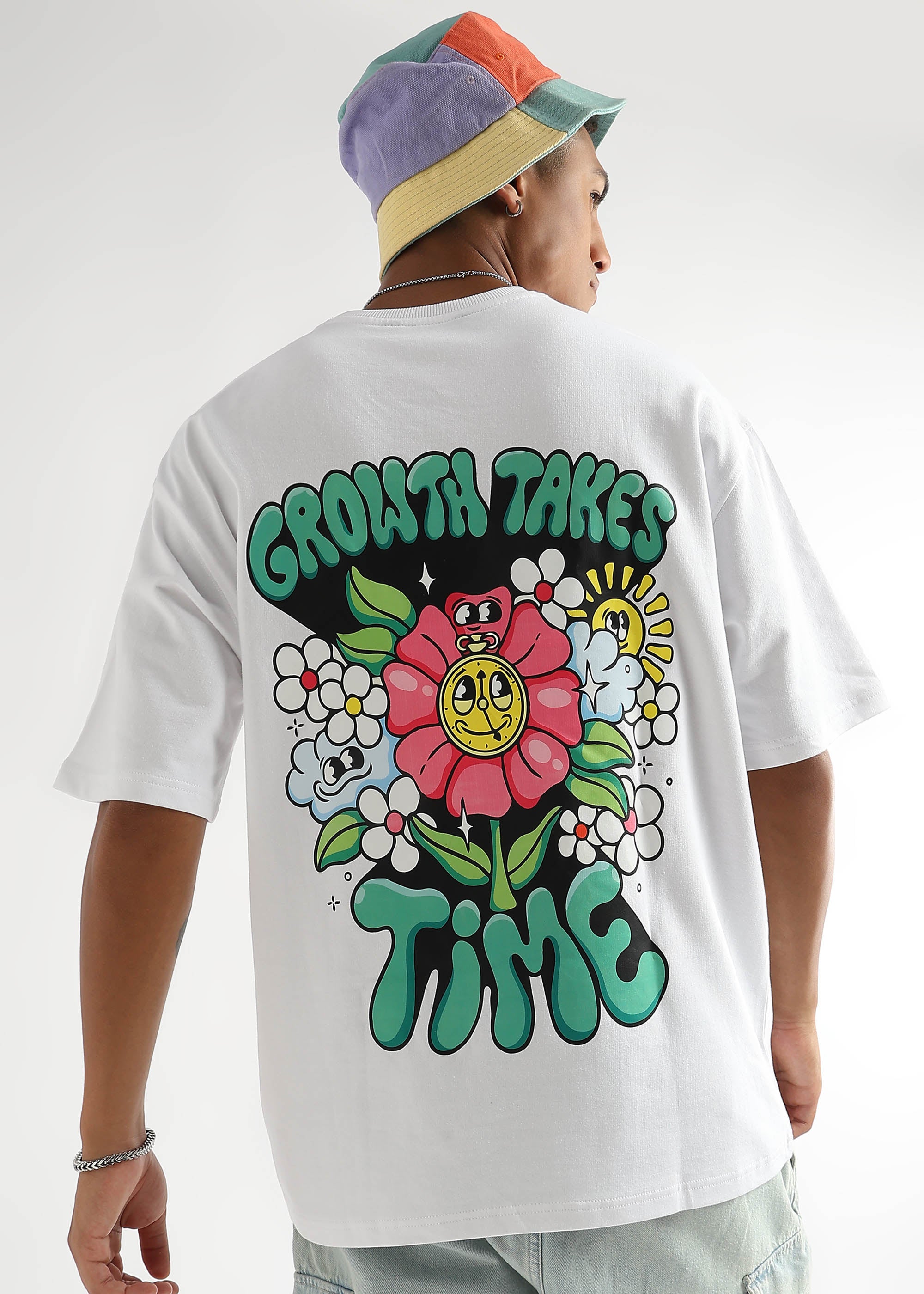 A person wearing a white oversized t-shirt with a floral graphic and the text 'GROWTH TAKES TIME' on the back.