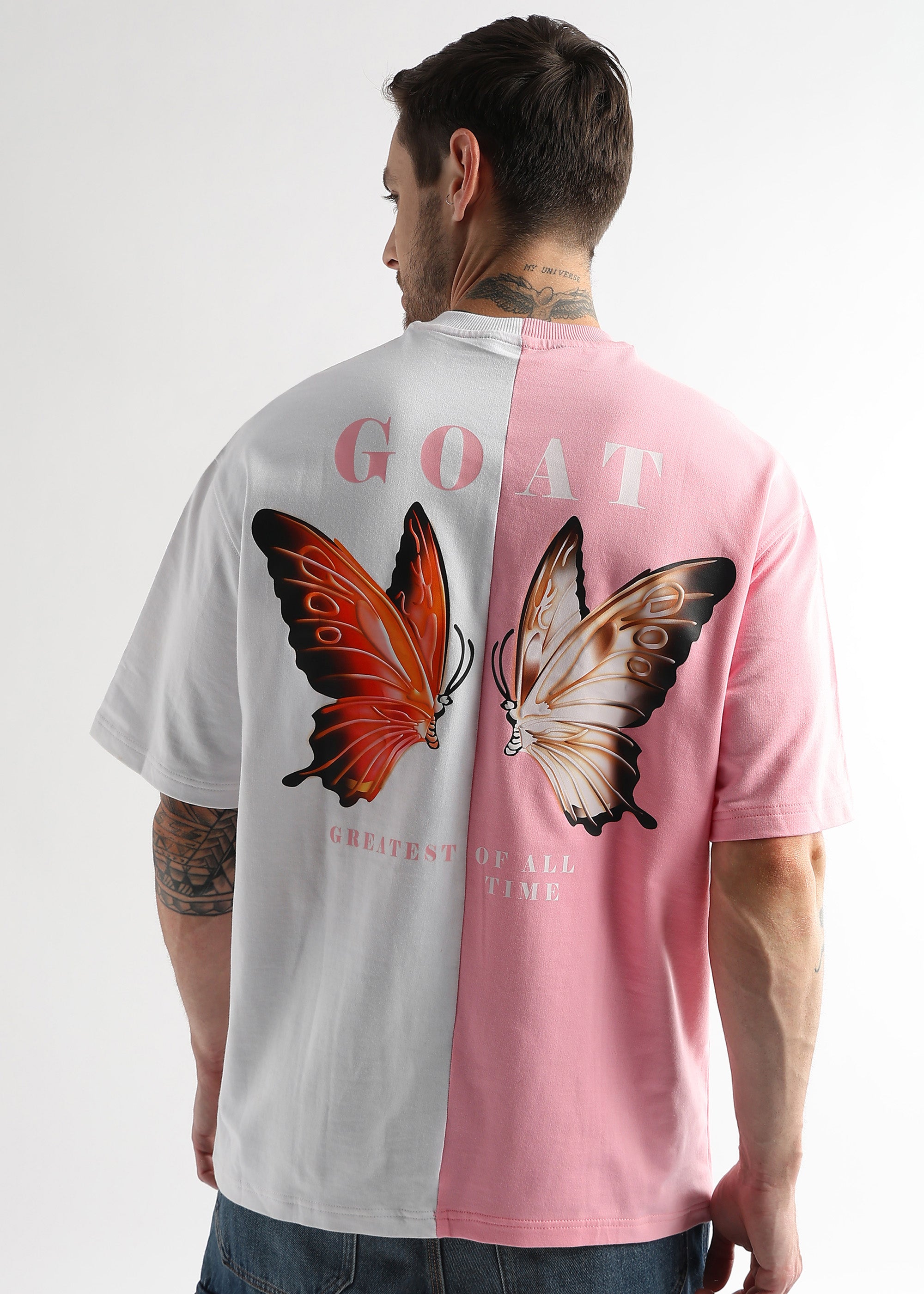 A person wearing an oversized t-shirt with a pink and white color combination and a graphic of two butterflies on the back, with the text 'GOAT' prominently displayed.