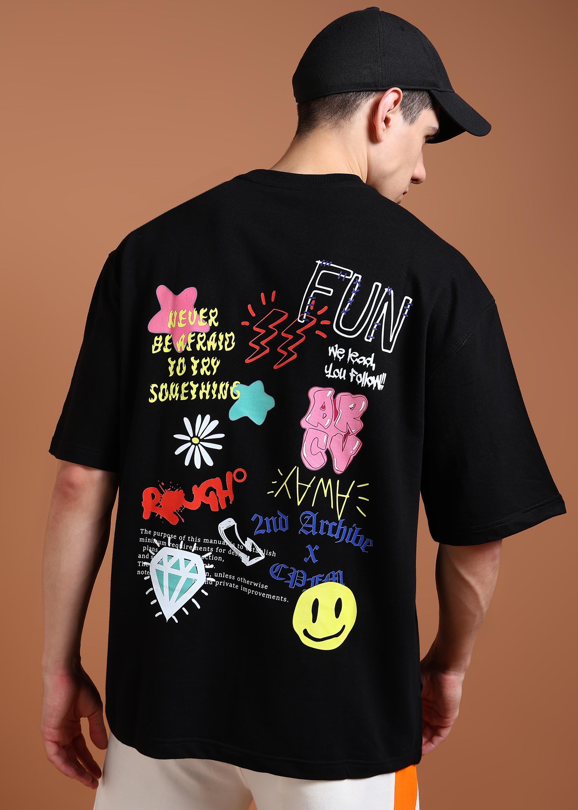 A person wearing a black oversized t-shirt with a colorful graphic design on the back, featuring text and various playful icons.