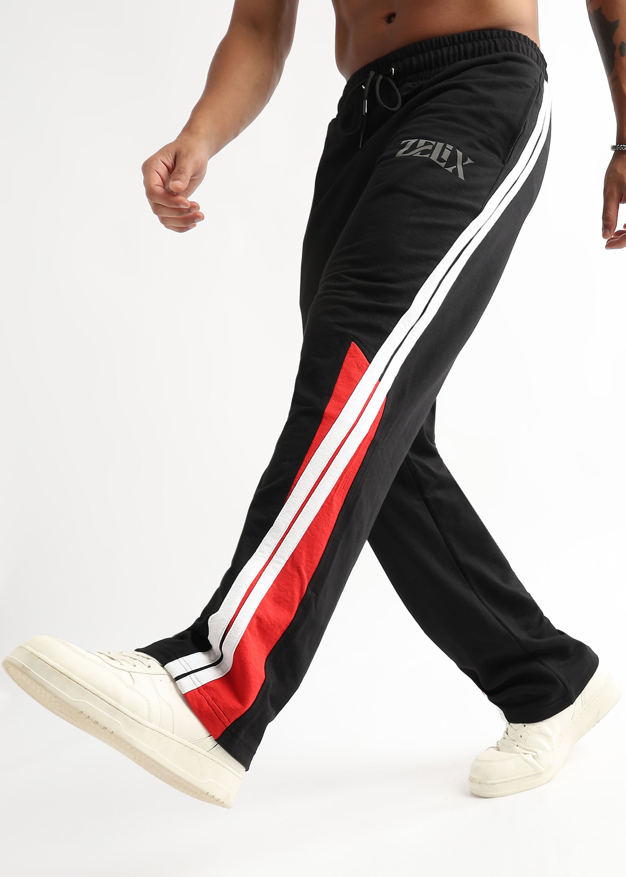 A person wearing black and red striped joggers with a white drawstring waistband and white sneakers.