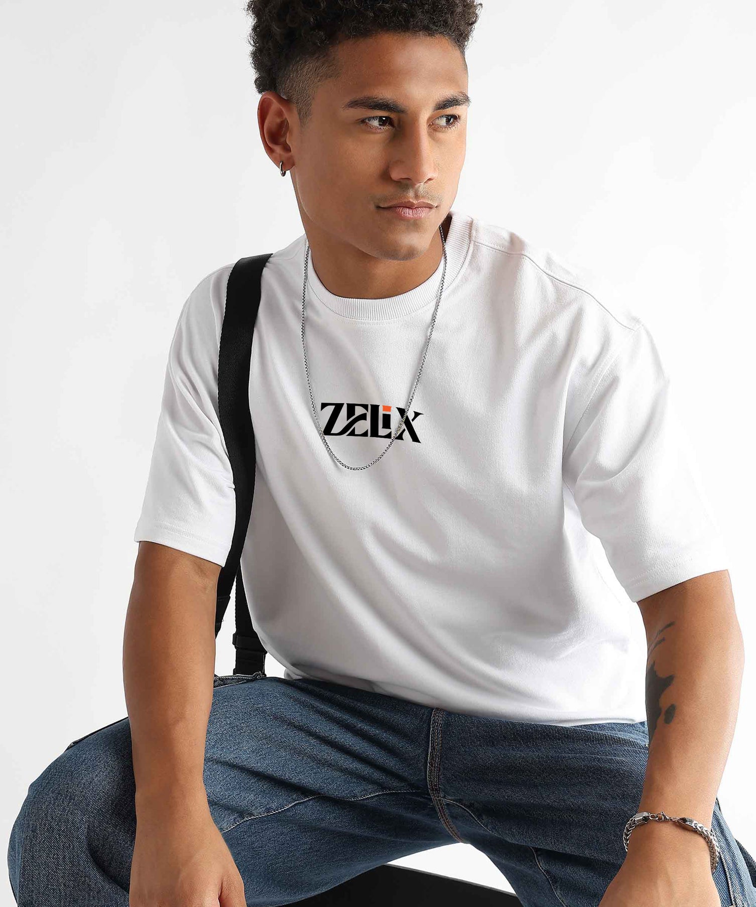 Man wearing a white t-shirt with a logo, sitting against a plain background