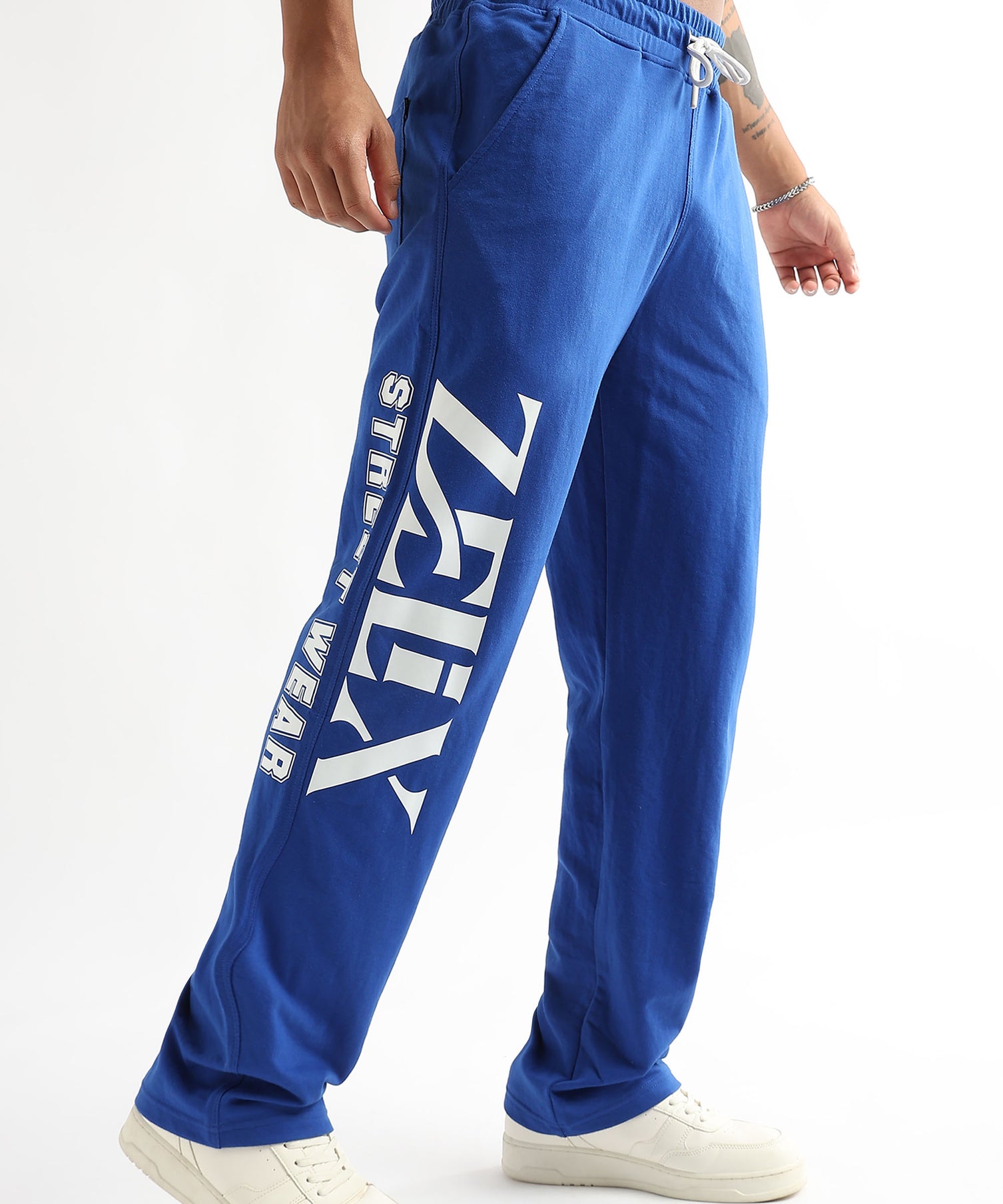 A person wearing royal blue joggers with the brand name 'ZELIX' written across the leg, paired with white sneakers.