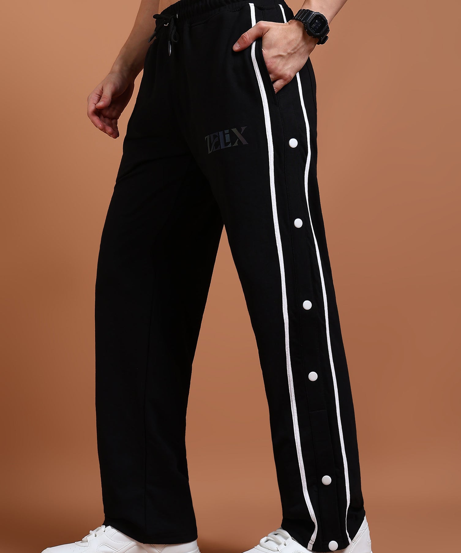 A person wearing black joggers with a white stripe and buttons on the side, paired with white sneakers.
