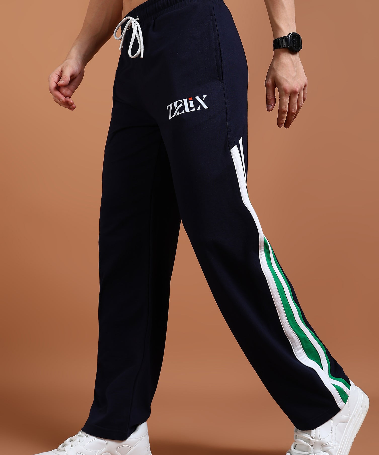 A person wearing navy blue and green baggy joggers with a drawstring waist, branded with 'ZELX' on the left leg, and white sneakers.