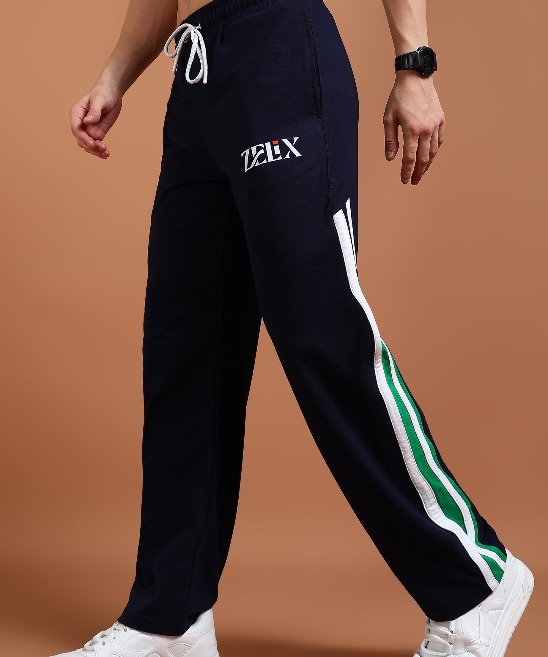 A person wearing navy blue and green baggy joggers with a drawstring waist, branded with 'ZELX' on the left leg, and white sneakers.