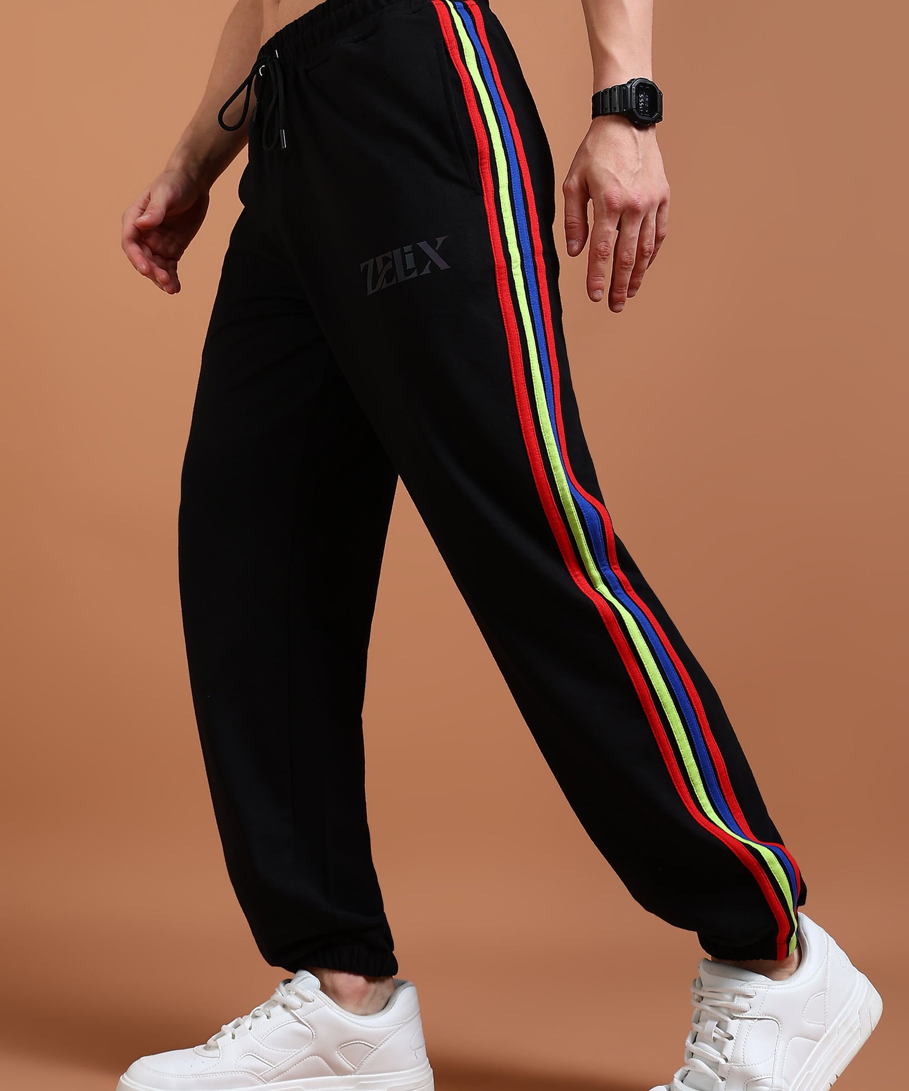 A person wearing black joggers with a multicolor stripe on the side and a drawstring waistband. The joggers have 'zelix' brand name on the left leg.