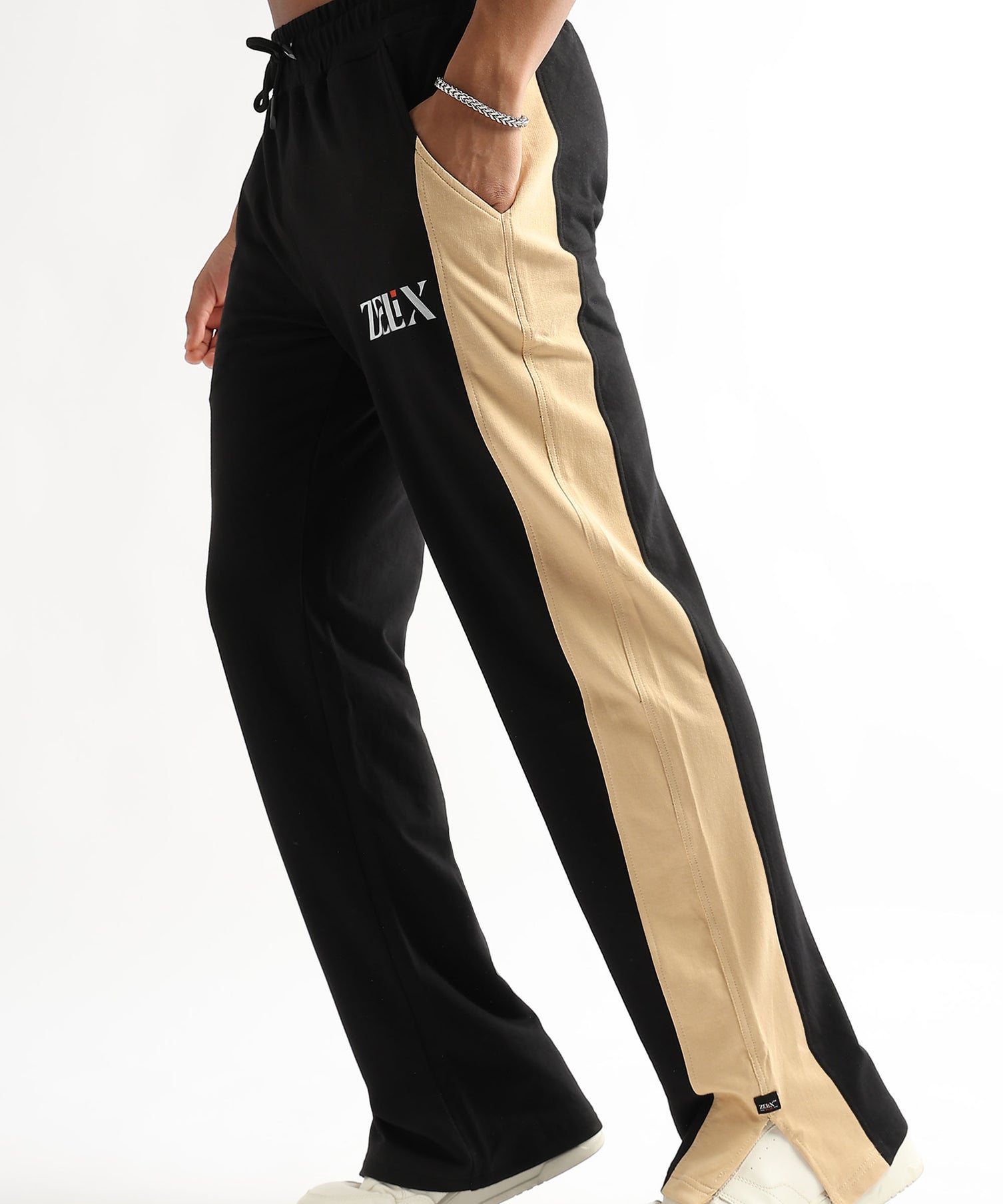 A person wearing black and beige side slit joggers with a drawstring waist, standing on one leg to showcase the side slit feature.