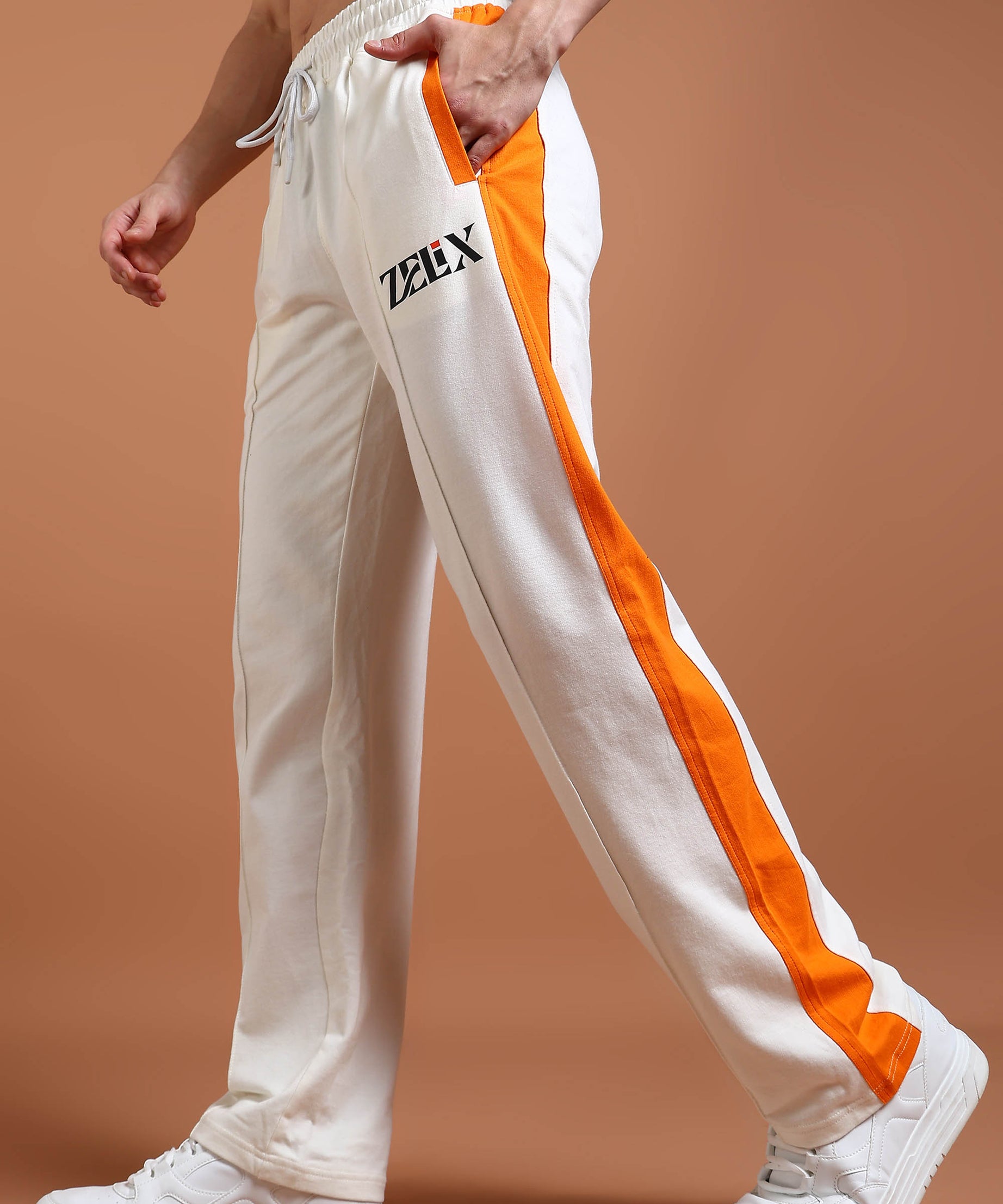 A pair of joggers with off-white and orange color contrast, featuring a drawstring waistband and a brand logo on the left leg.