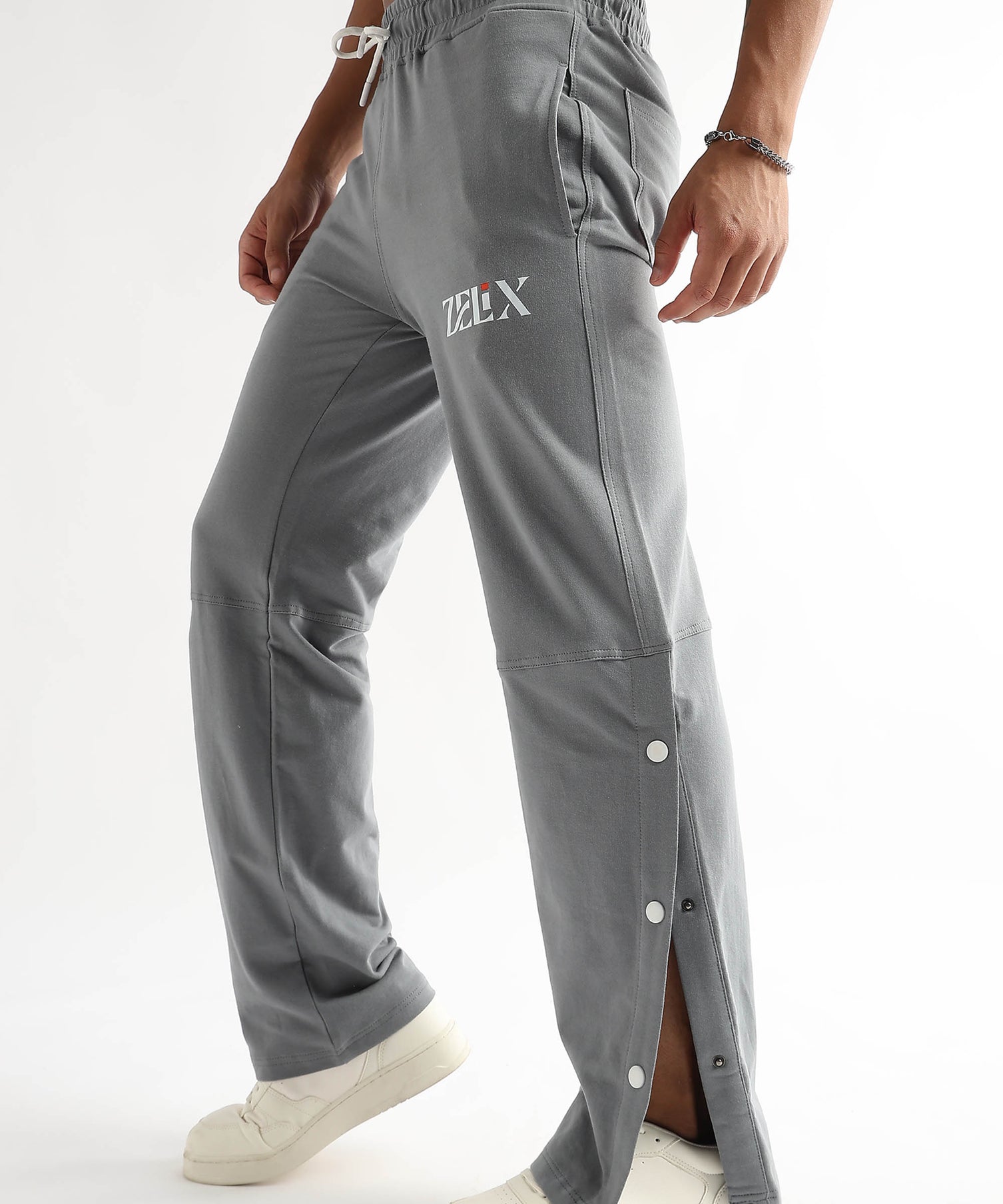 A person wearing grey baggy joggers with a drawstring waistband and side snap details, paired with white sneakers.