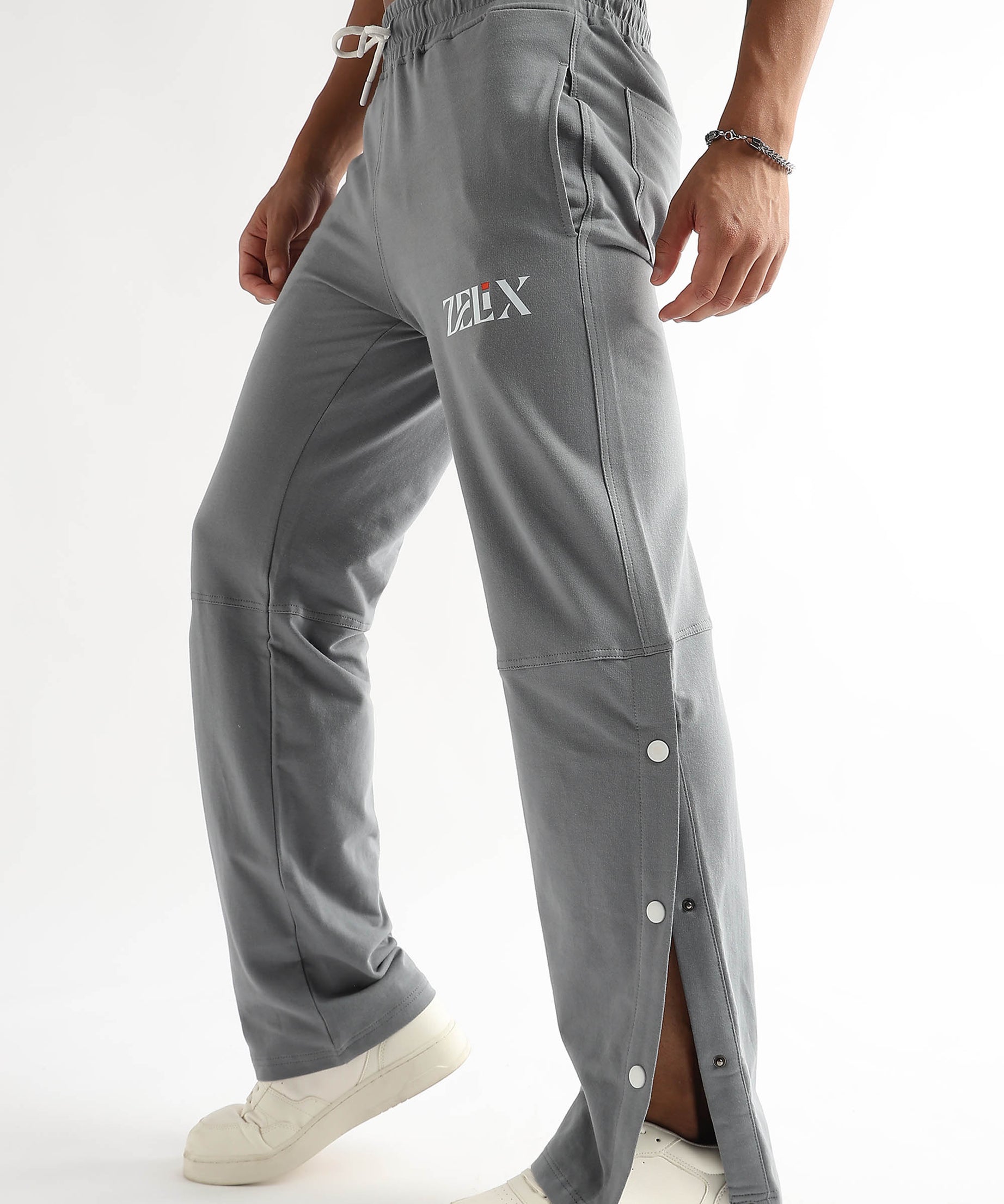 A person wearing grey baggy joggers with a drawstring waistband and side snap details, paired with white sneakers.