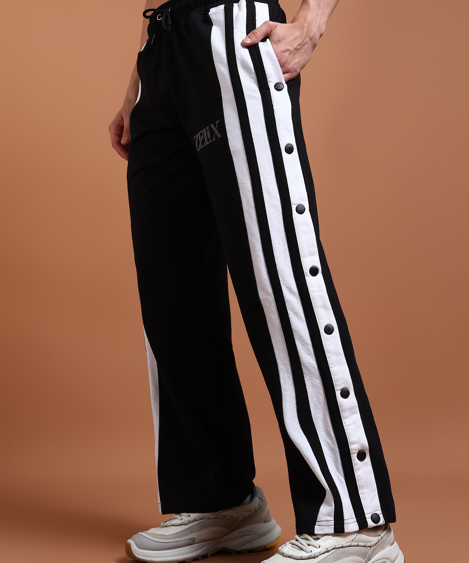 A person wearing black unisex joggers with white stripes and buttons on the side, paired with a black top and white sneakers.