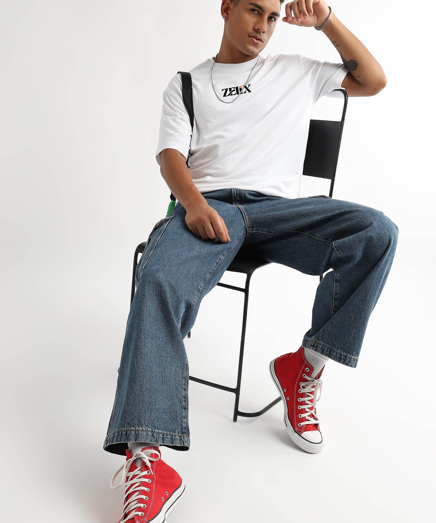 Person sitting on a chair wearing a white t-shirt, blue jeans, and red sneakers.