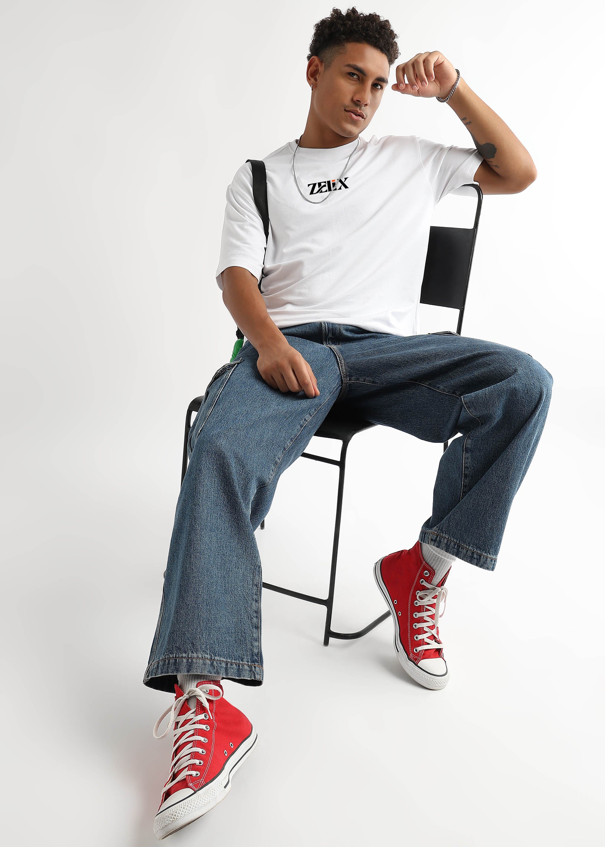 Person sitting on a chair wearing a white t-shirt, blue jeans, and red sneakers.