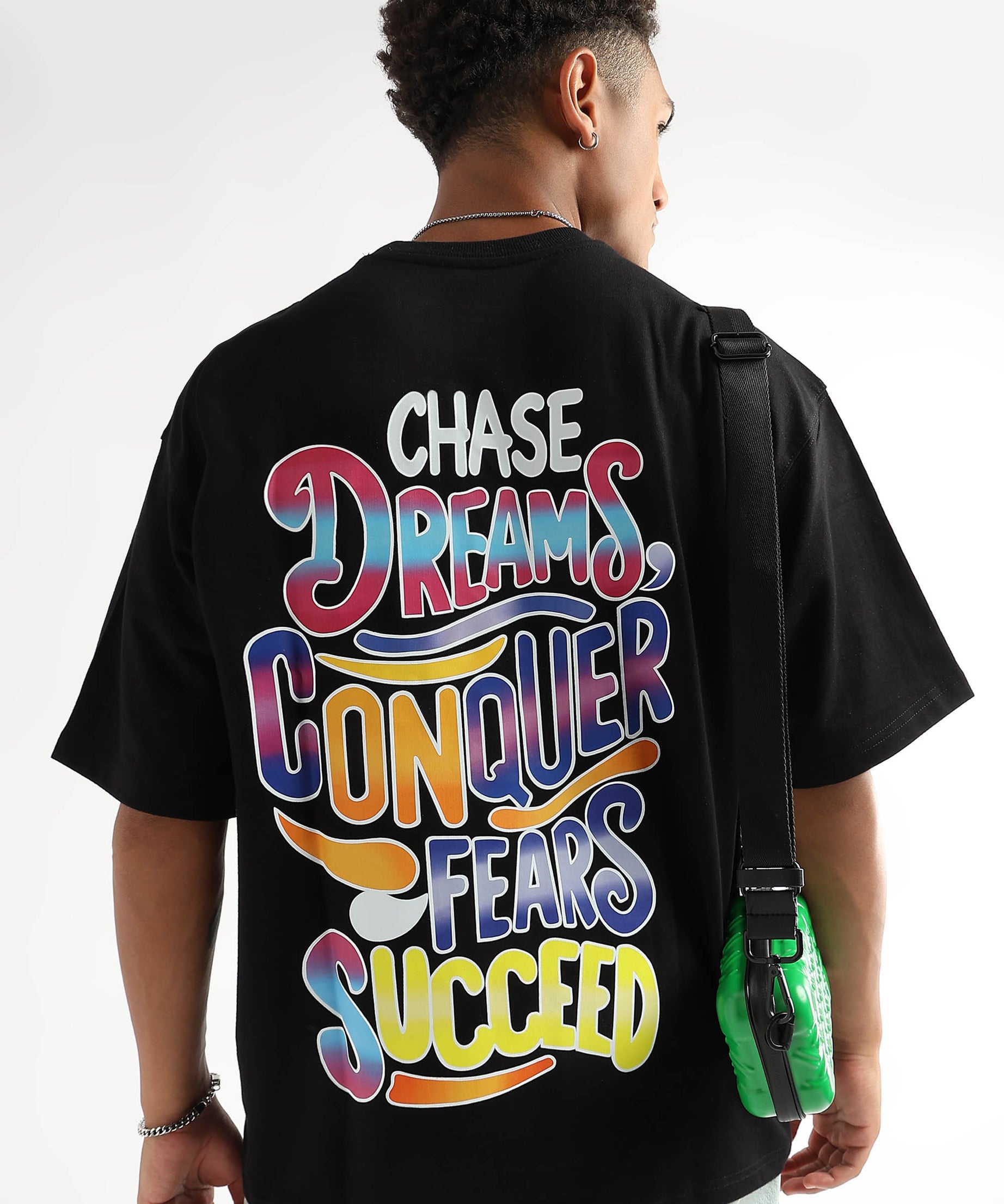 A person wearing an oversized black t-shirt with a bold graphic on the back that reads 'CHASE DREAMS, CONQUER FEARS, SUCCEED' in multicolored letters.
