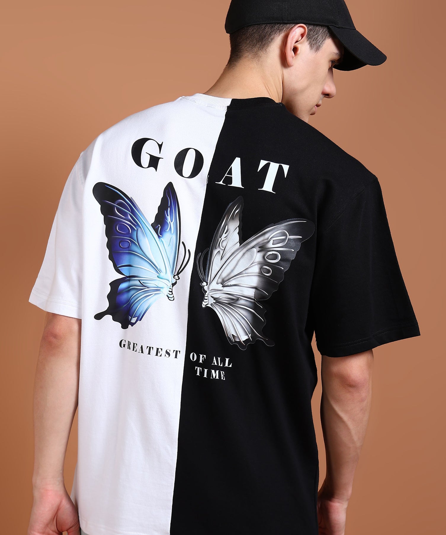 A person wearing an oversized black and white t-shirt with a graphic of a butterfly and the text 'GOAT' on the back.