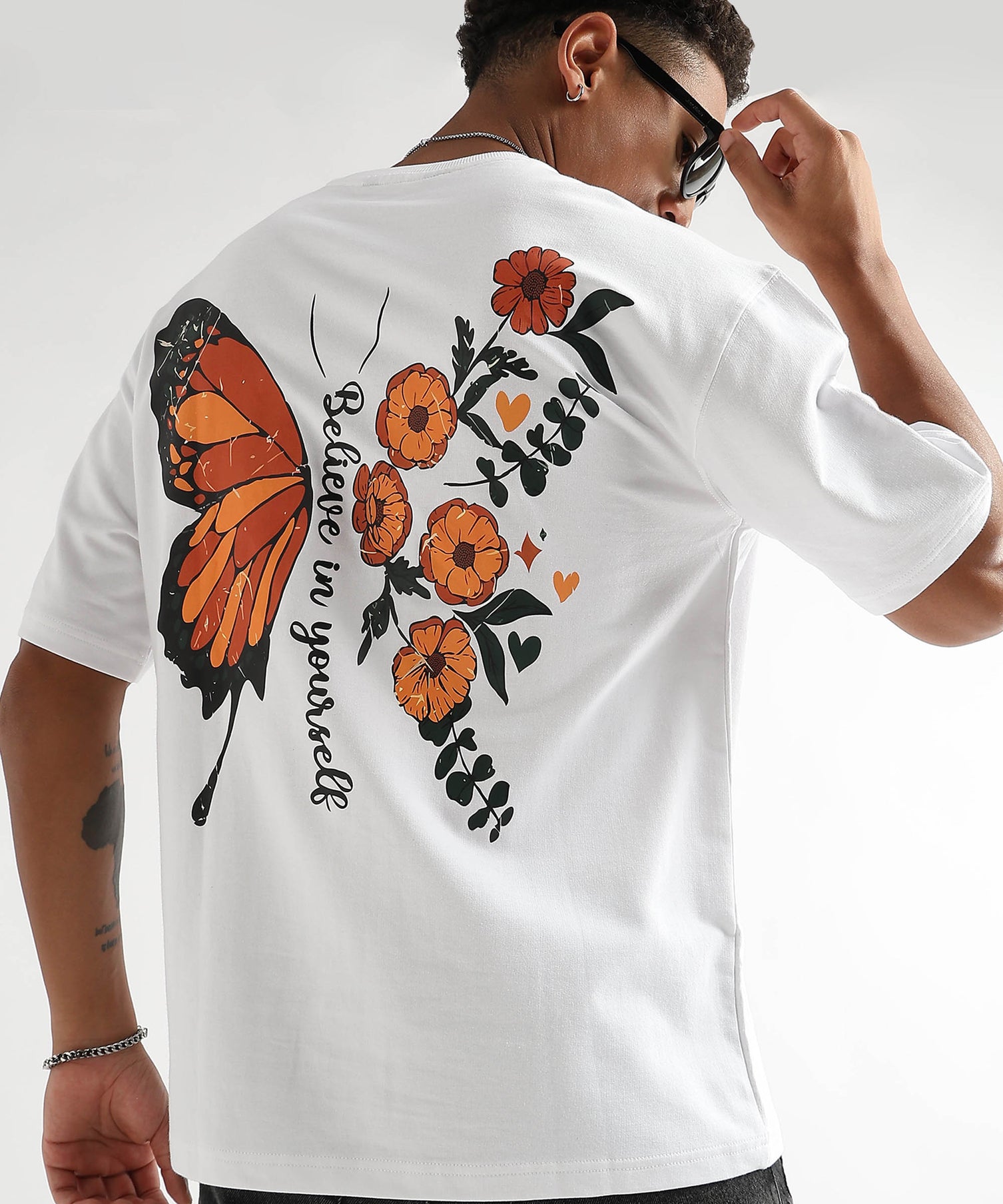 A person wearing an oversized white t-shirt with a graphic of a butterfly and flowers on the back.