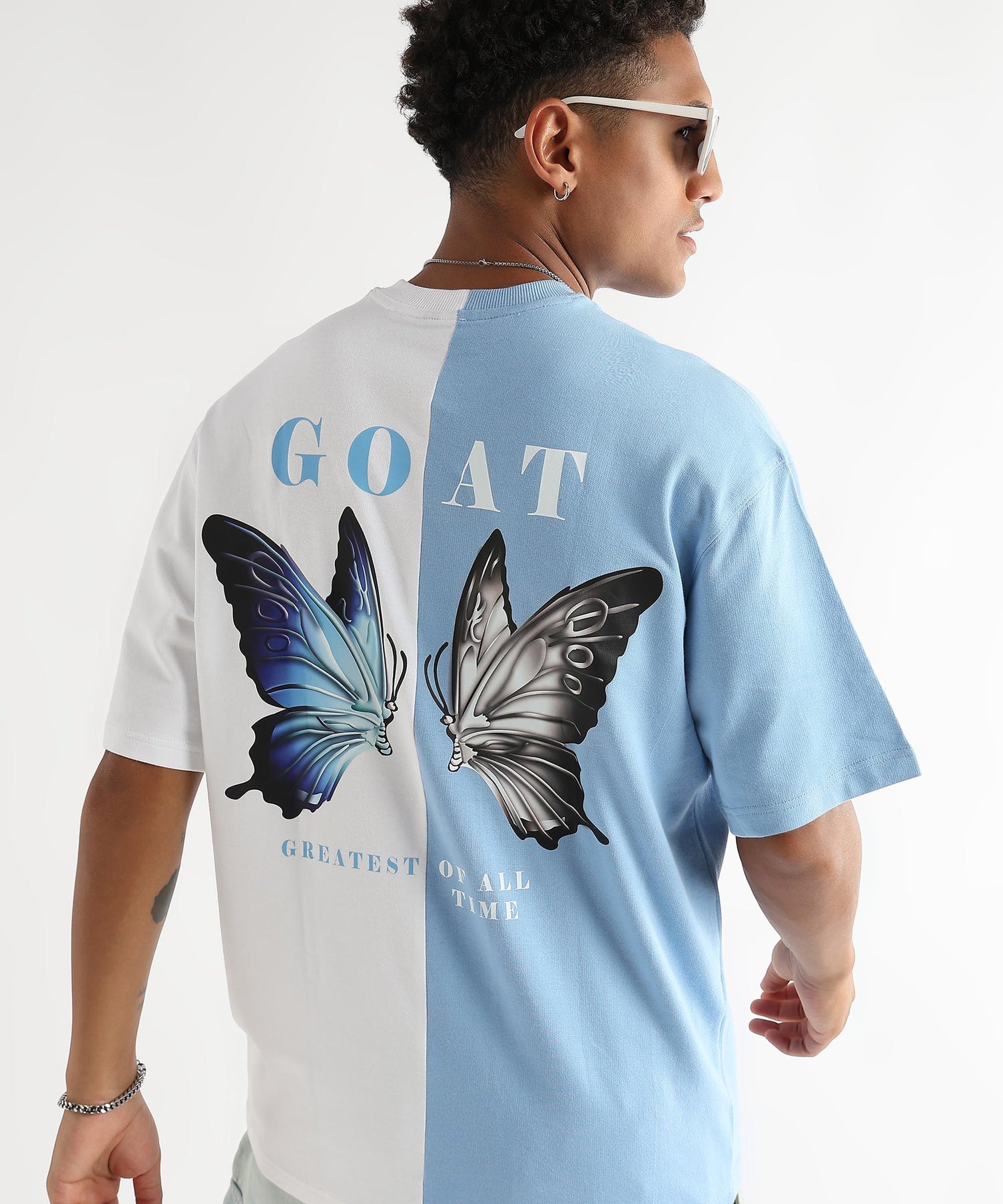 A person wearing an oversized t-shirt with a sky blue and white color scheme. The shirt has a graphic of two butterflies and the text 'GOAT' on the back.
