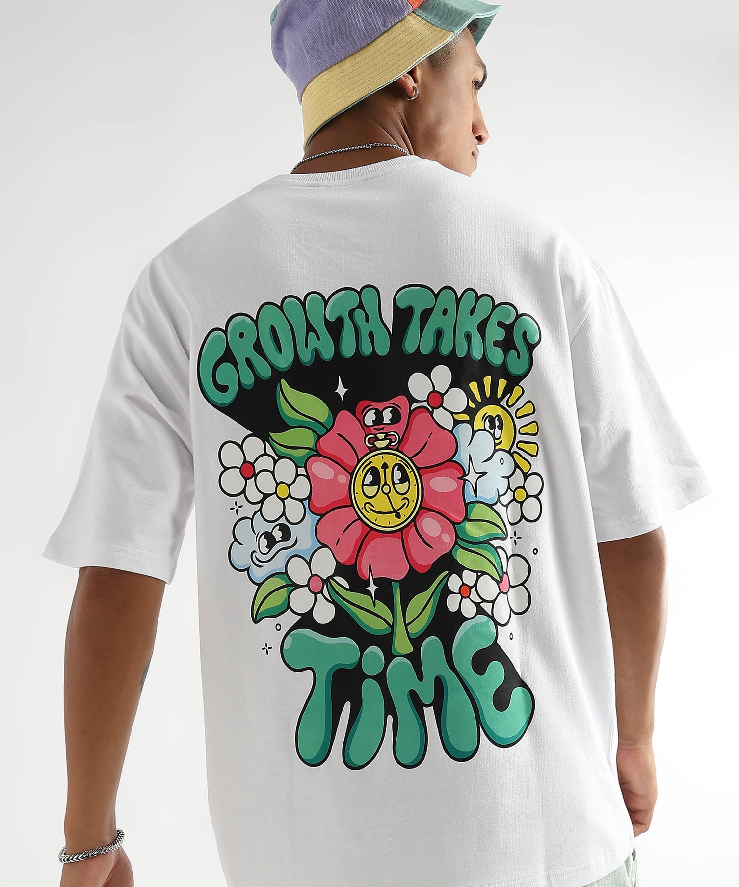 A person wearing a white oversized t-shirt with a floral graphic and the text 'GROWTH TAKES TIME' on the back.