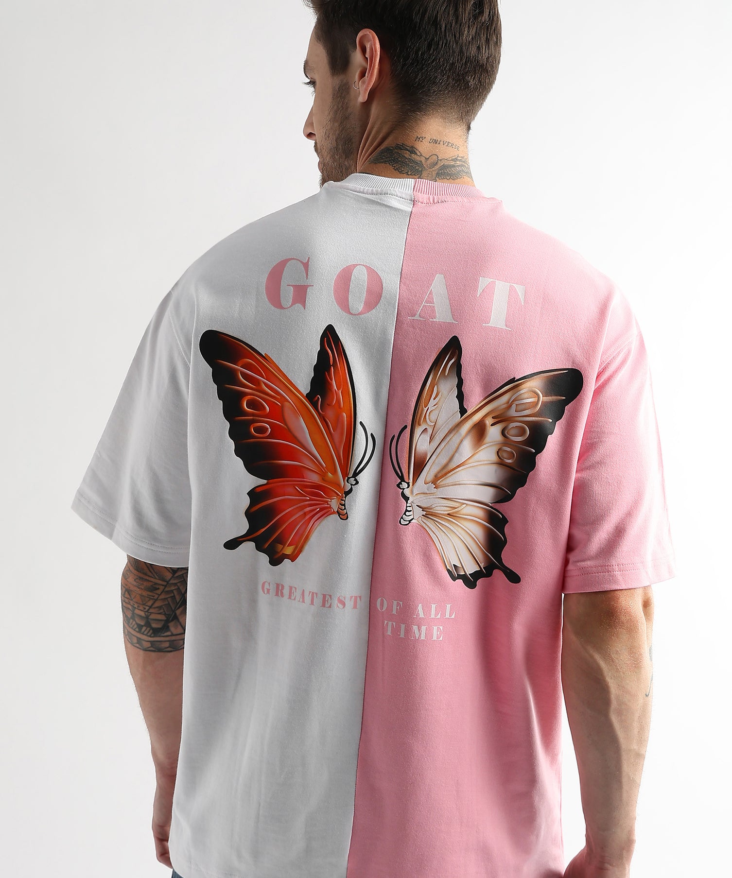 A person wearing an oversized t-shirt with a pink and white color combination and a graphic of two butterflies on the back, with the text 'GOAT' prominently displayed.