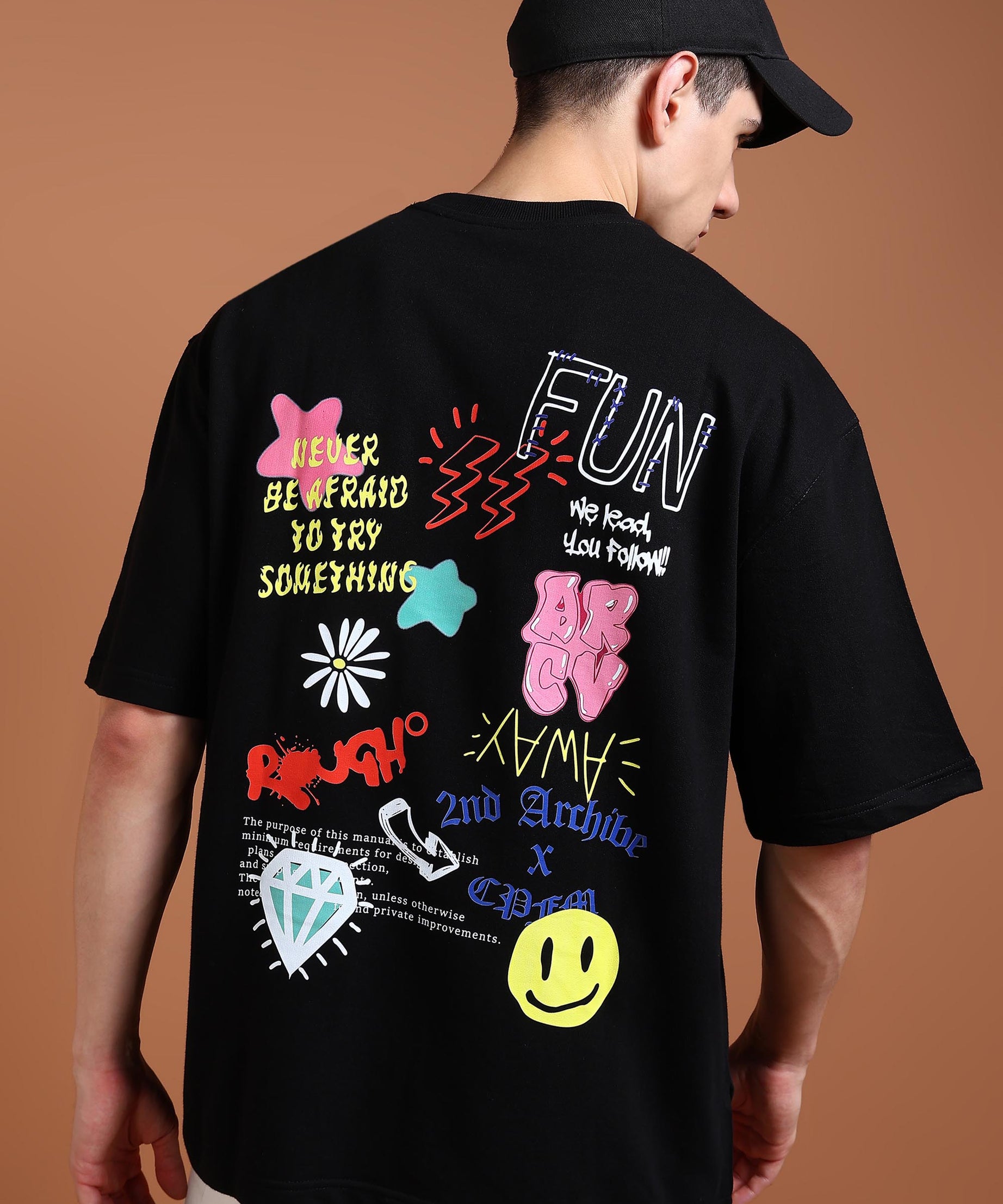 A person wearing a black oversized t-shirt with a colorful graphic design on the back, featuring text and various playful icons.