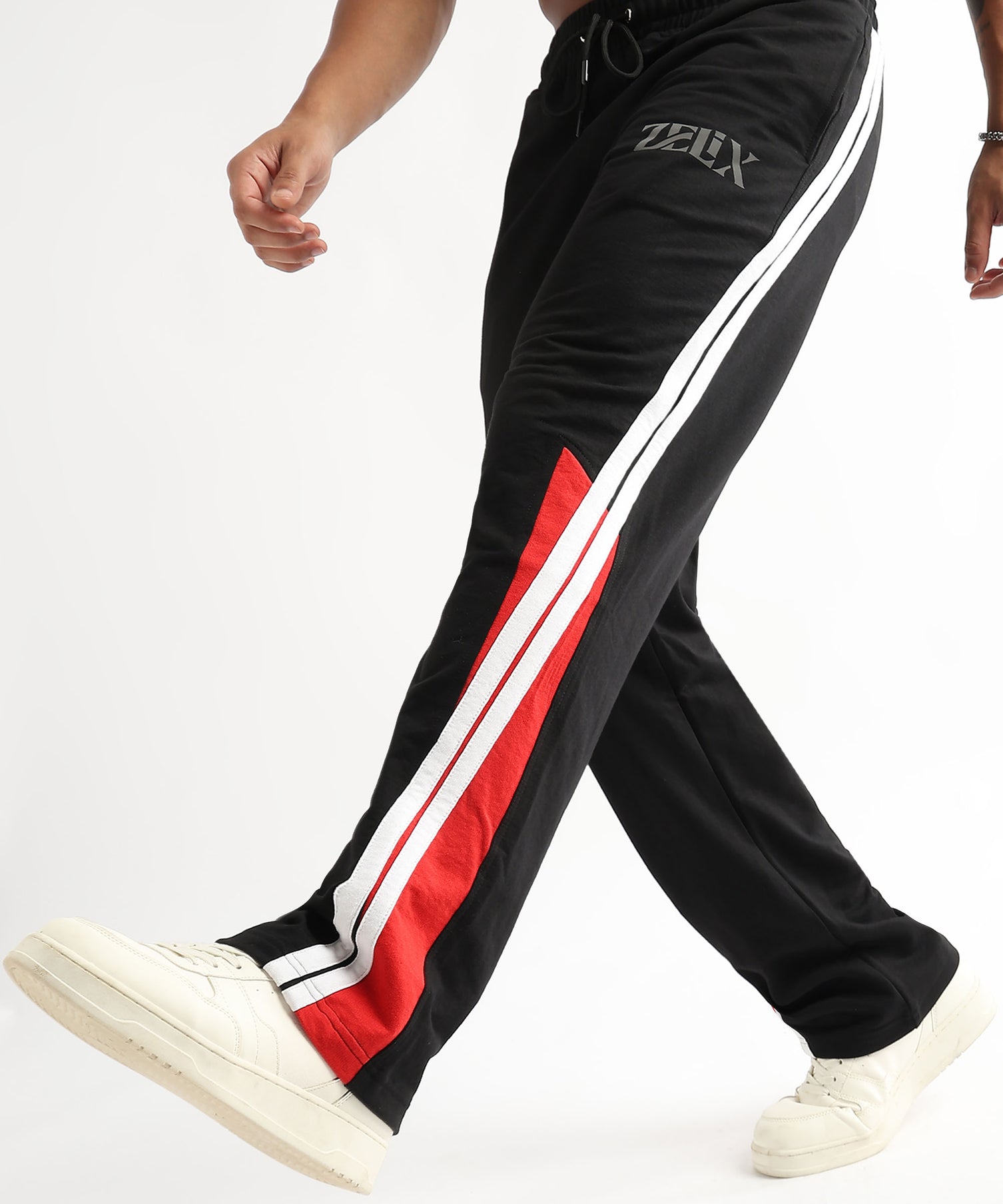 A person wearing black and red striped joggers with a white drawstring waistband and white sneakers.